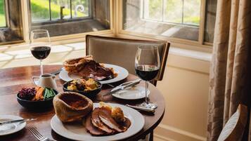 A dining table with plates of food, a glass of red wine, and a pitcher.