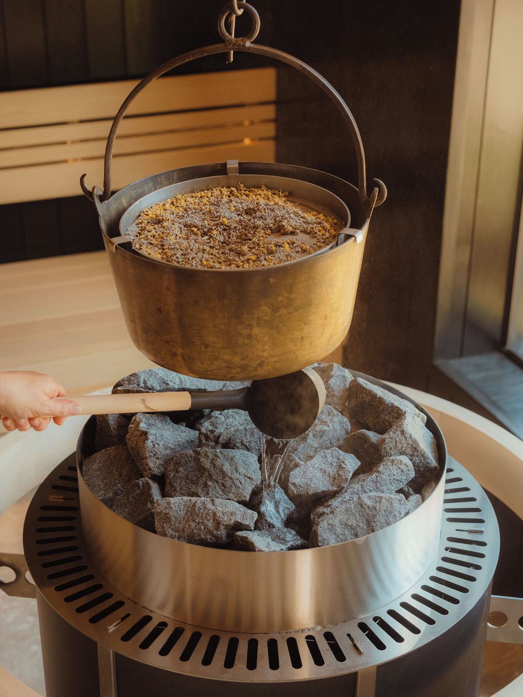 Una instalación para cocinar con una olla sobre una parrilla, una cuchara para servir y una persona removiendo.