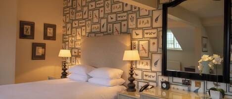 A hotel room with a bed, bedside lamps, a dresser, a mirror, and a wall decorated with framed pictures.