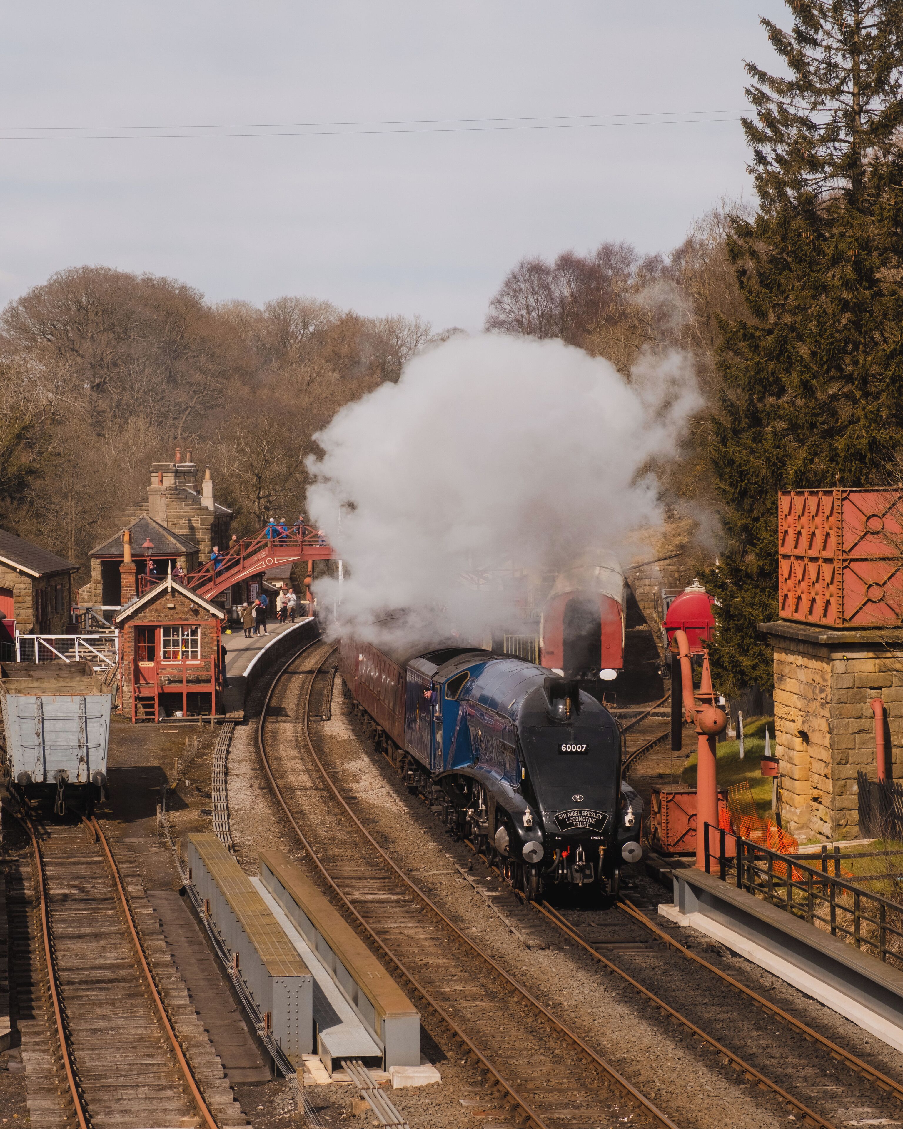 A steam locomotive on a curved railway track with a station platform and buildings in the background.