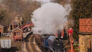 A steam locomotive on a curved railway track with a station platform and buildings in the background.