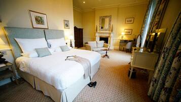 A hotel room with a large bed, a desk, a chair, a fireplace, and a mirror.