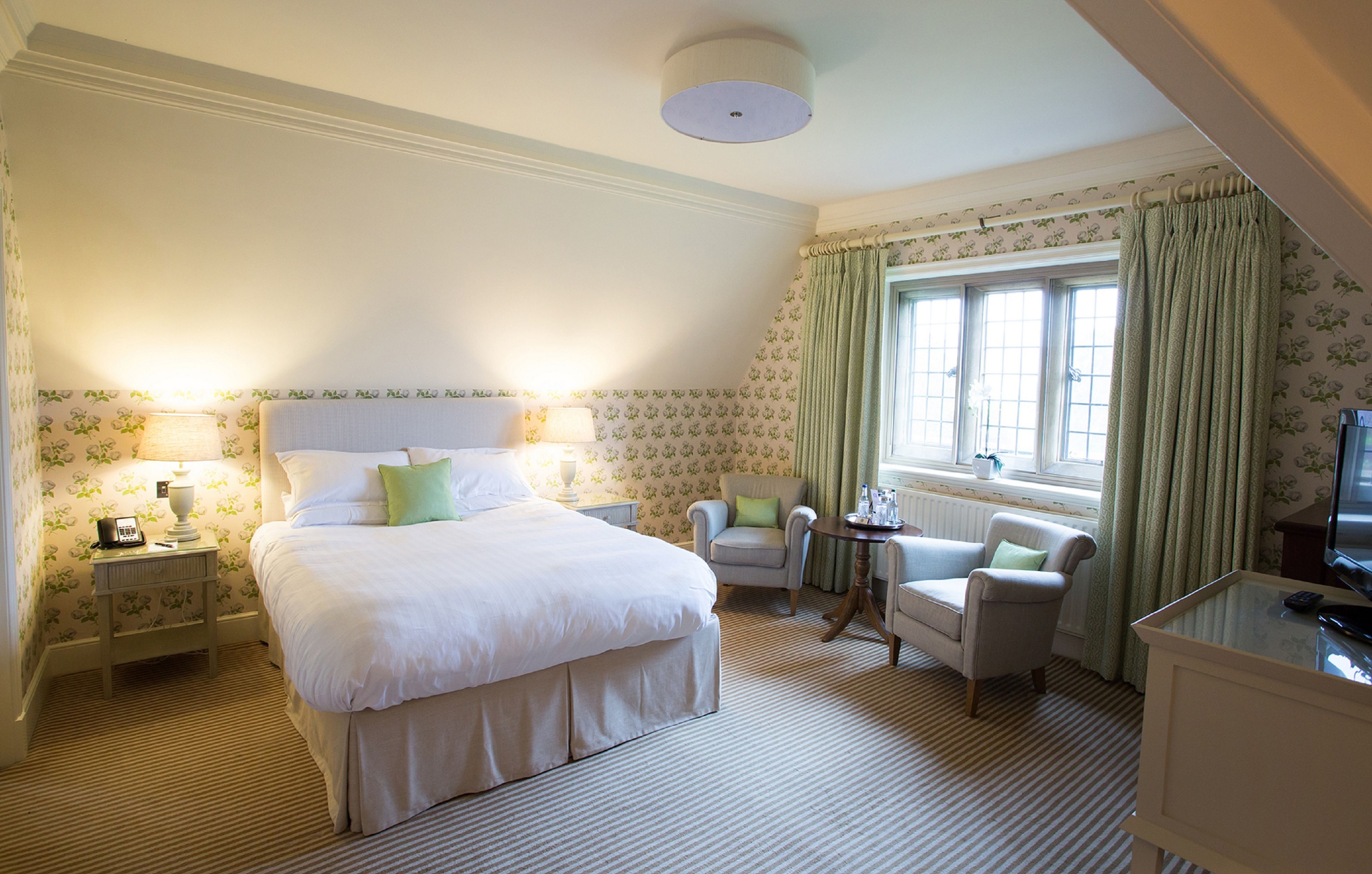 A hotel room with a large bed, two armchairs, a small table, a television, and a window with curtains.