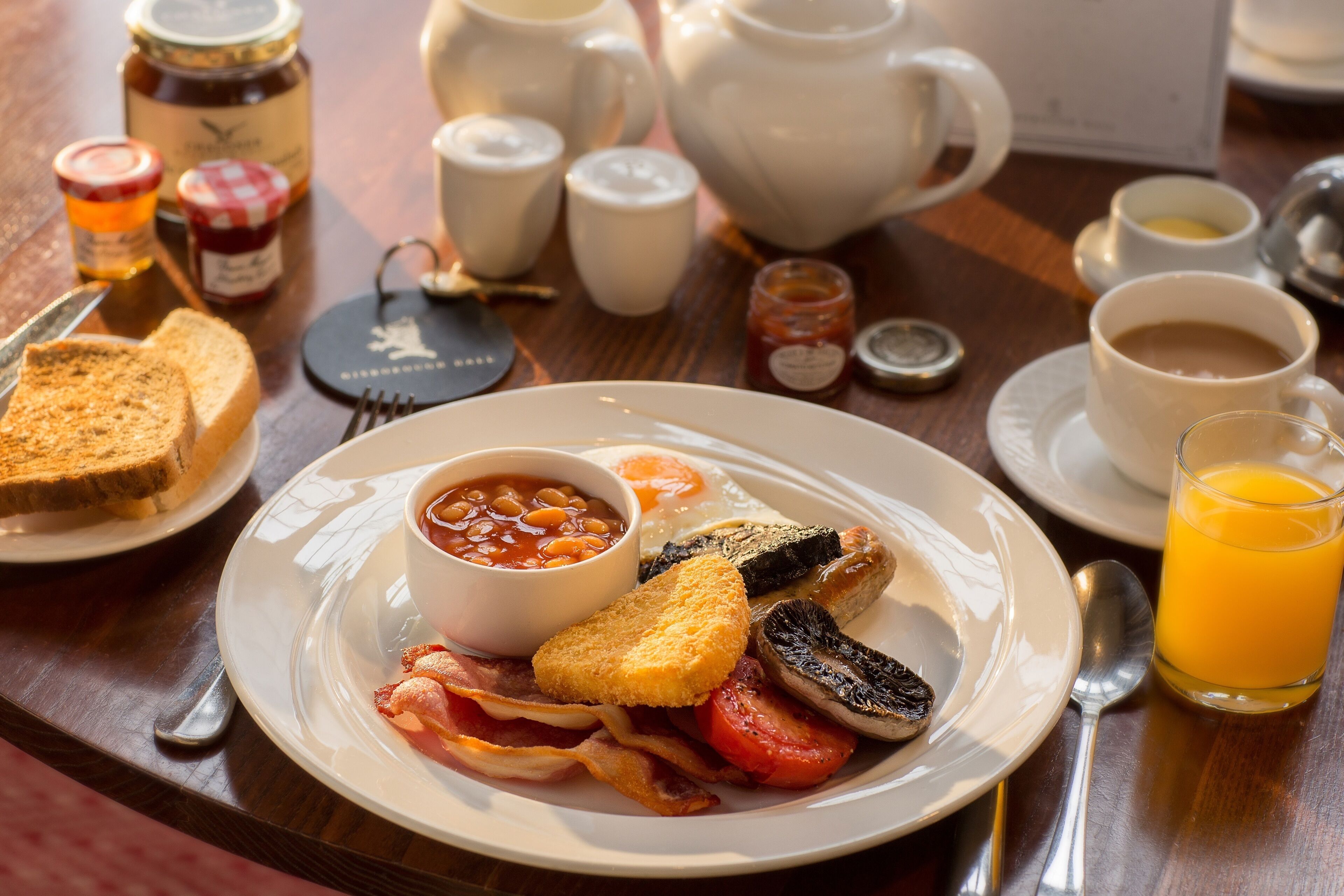 A breakfast plate with toast, beans, eggs, bacon, mushrooms, and a glass of orange juice.