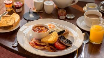 A breakfast plate with toast, beans, eggs, bacon, mushrooms, and a glass of orange juice.