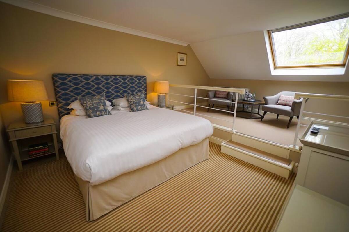 A hotel room with a large bed, a desk, a chair, a lamp, and a window.