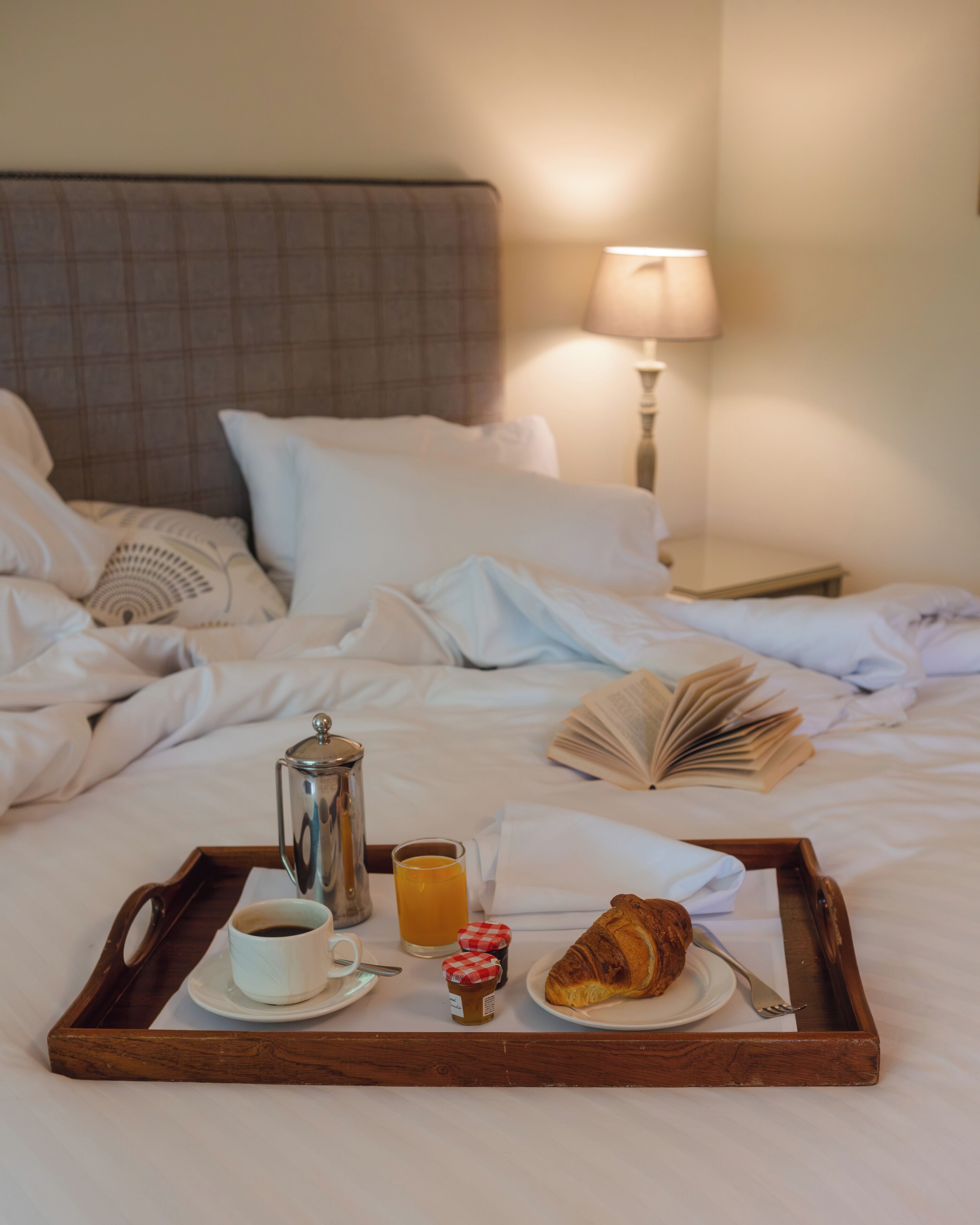 A neatly made bed with a tray of breakfast items including coffee, juice, a croissant, and a pastry.