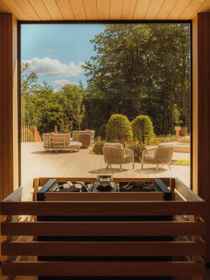 Vista desde una habitación con un ventanal grande que da a un área de estar exterior con sillas y una chimenea.