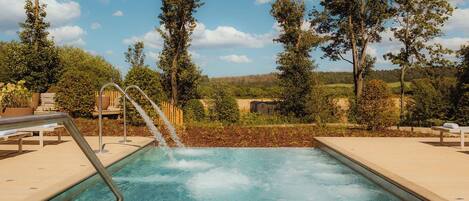 A pool with a waterfall feature surrounded by trees and a clear sky.