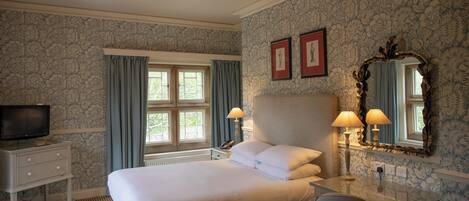 A hotel room with a large bed, two bedside lamps, a desk with a chair, a television, and a window with curtains.