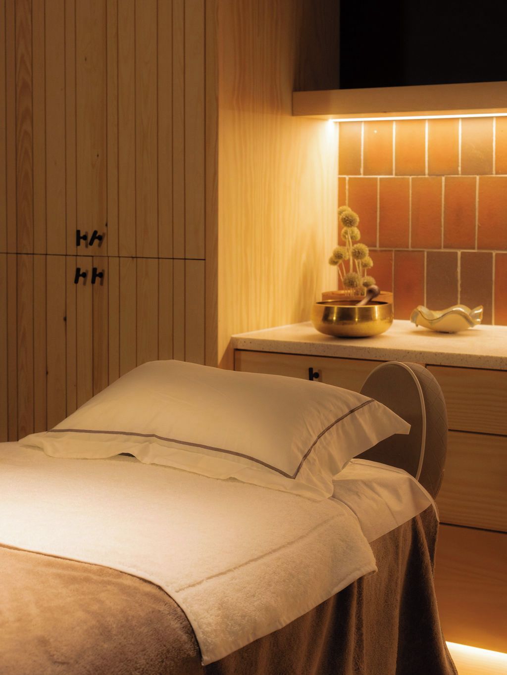 A bedroom with a bed, a nightstand, a bowl with a plant, and a wall with a pattern.