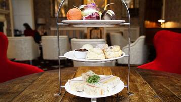 A three-tiered dessert stand with various pastries and a sandwich on a wooden table in a dining area.