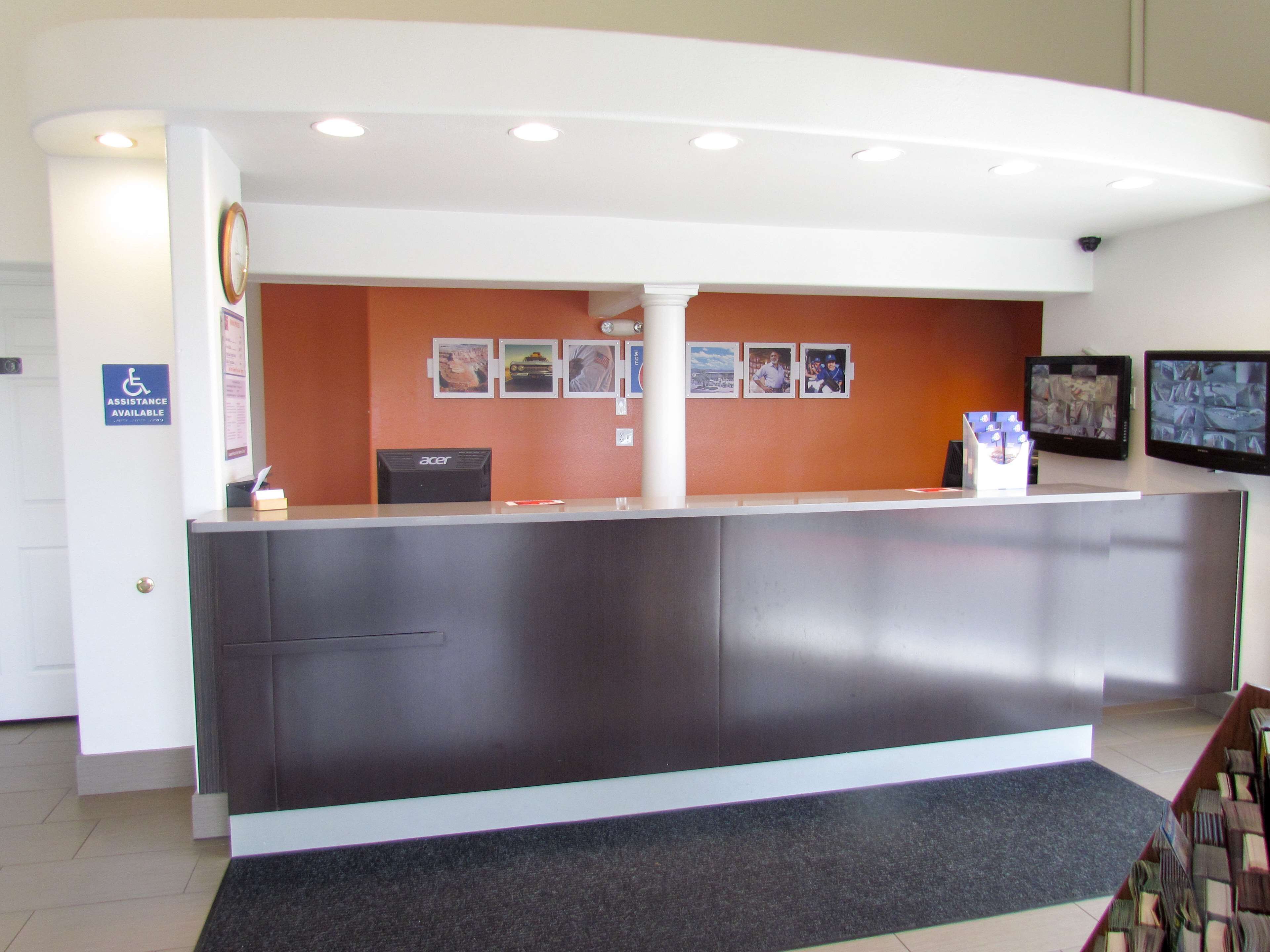 A reception desk with a computer, a clock, and a sign indicating assistance is available.