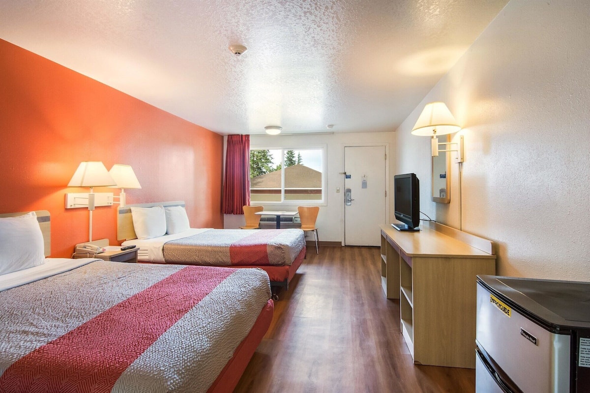 A hotel room with two beds, a desk with a computer, a television, and a refrigerator.
