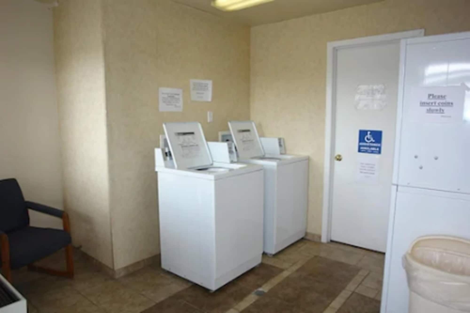 A laundry room with two washing machines and a dryer, a wheelchair-accessible door, and a trash can.