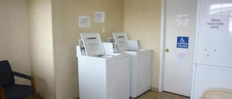 A laundry room with two washing machines and a dryer, a wheelchair-accessible door, and a trash can.