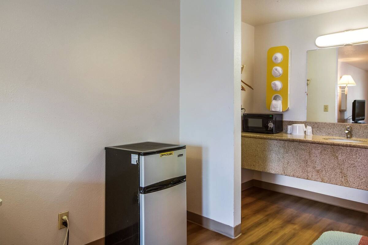 A compact kitchenette with a refrigerator, microwave, and a sink with a mirror above.