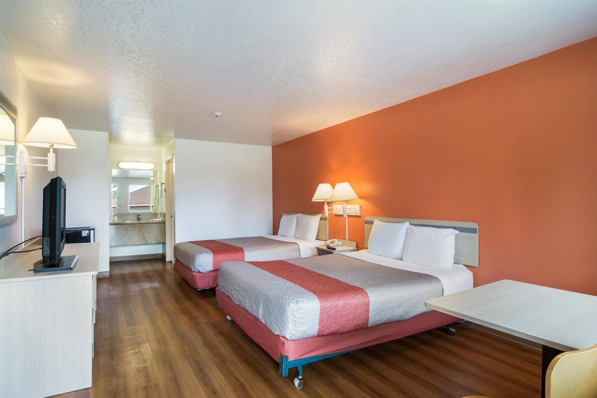 A hotel room with two beds, a desk, a TV, and a bathroom visible through an open door.