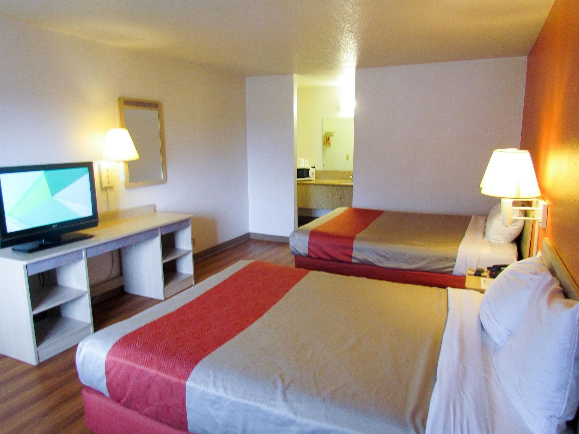 A hotel room with two beds, a desk with a computer, and a mirror.