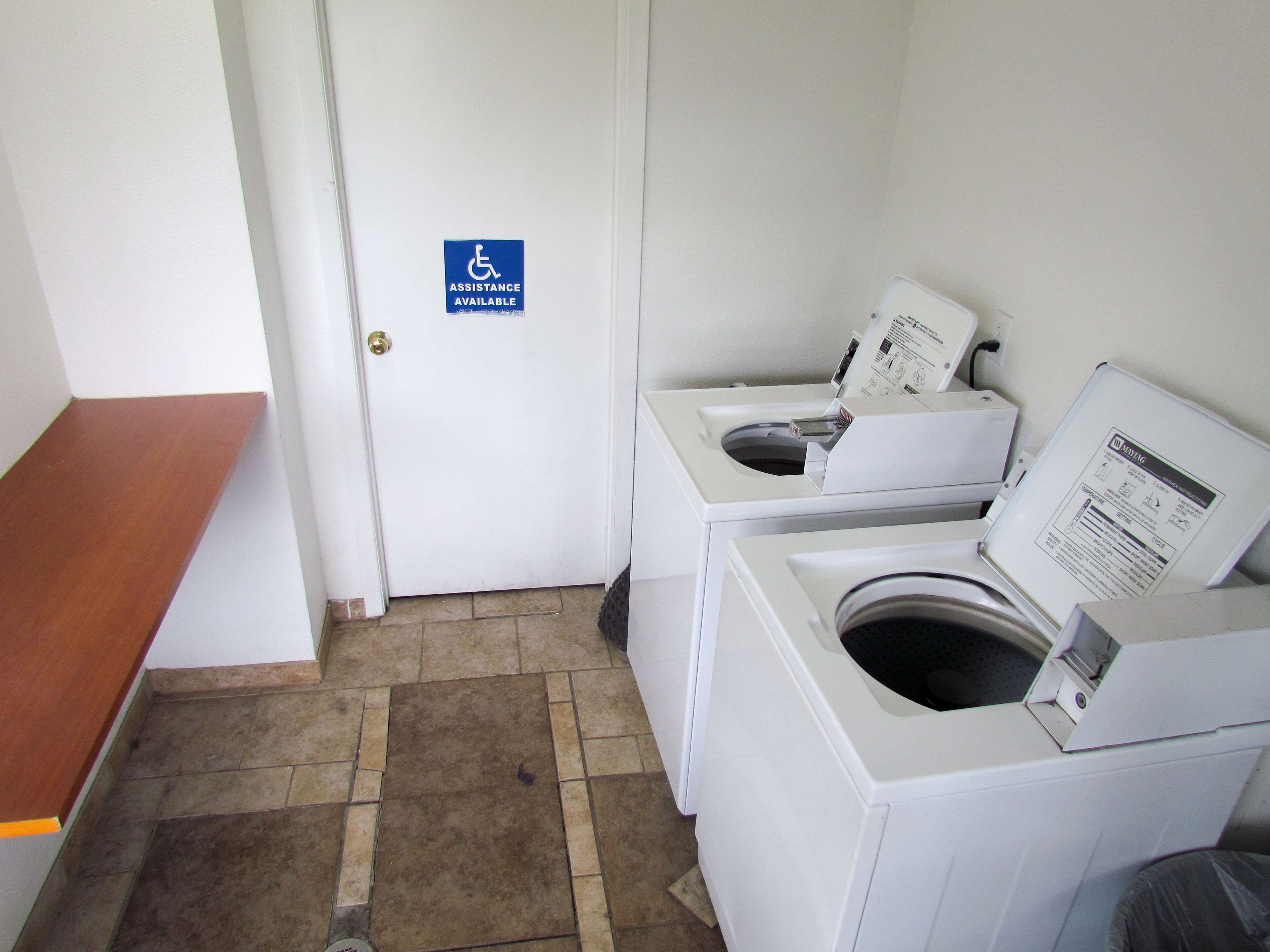 A laundry room with a door marked "ASSISTANCE AVAILABLE" and a bench.