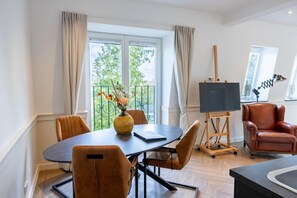 Een moderne woonkamer met een eethoek, een televisie op een dressoir, een leren fauteuil en een balkon met uitzicht.
