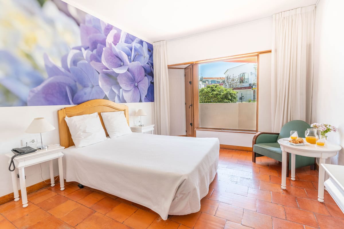 A hotel room with a large bed, a small table with a lamp, a chair, and a view of the outside.