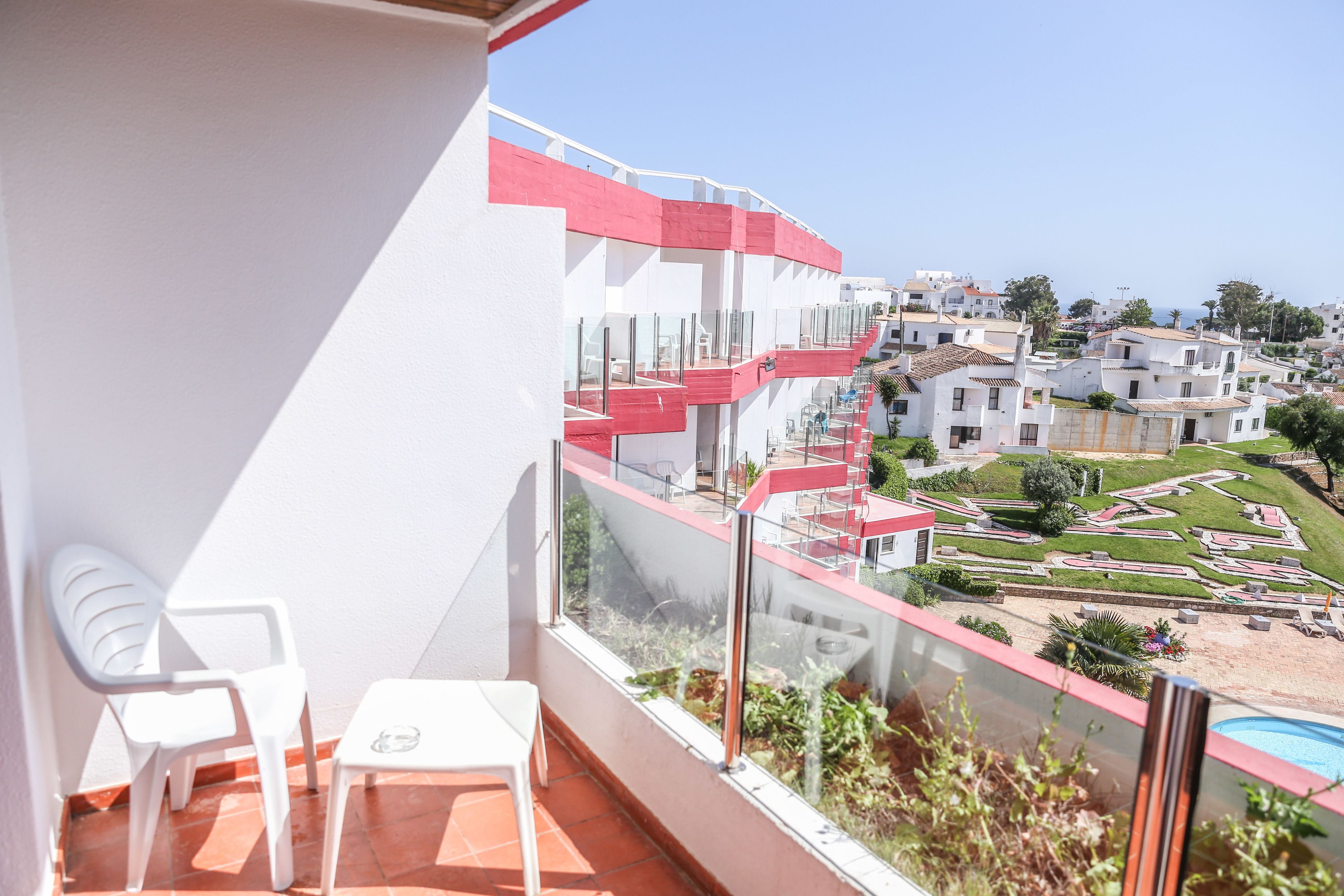 A balcony with a view of a residential area, white chairs, and a glass railing.