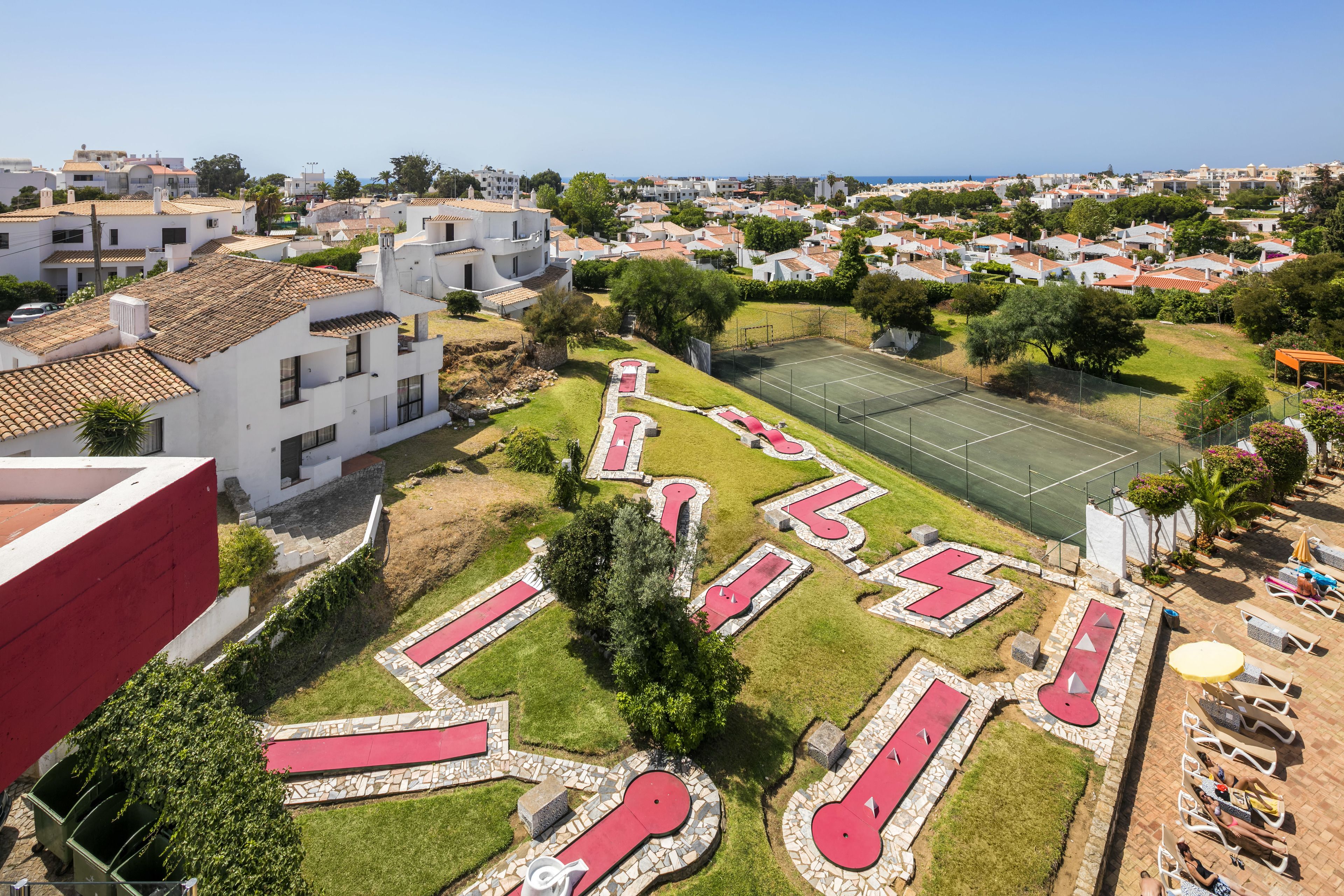 A residential area with a tennis court, a swimming pool, and a red-roofed building.