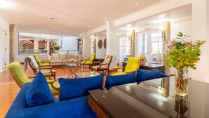 A spacious living area with a large blue sofa, yellow and green chairs, a glass coffee table, and a vase with flowers. - Hotel da Aldeia - Adults Only (Albufeira)