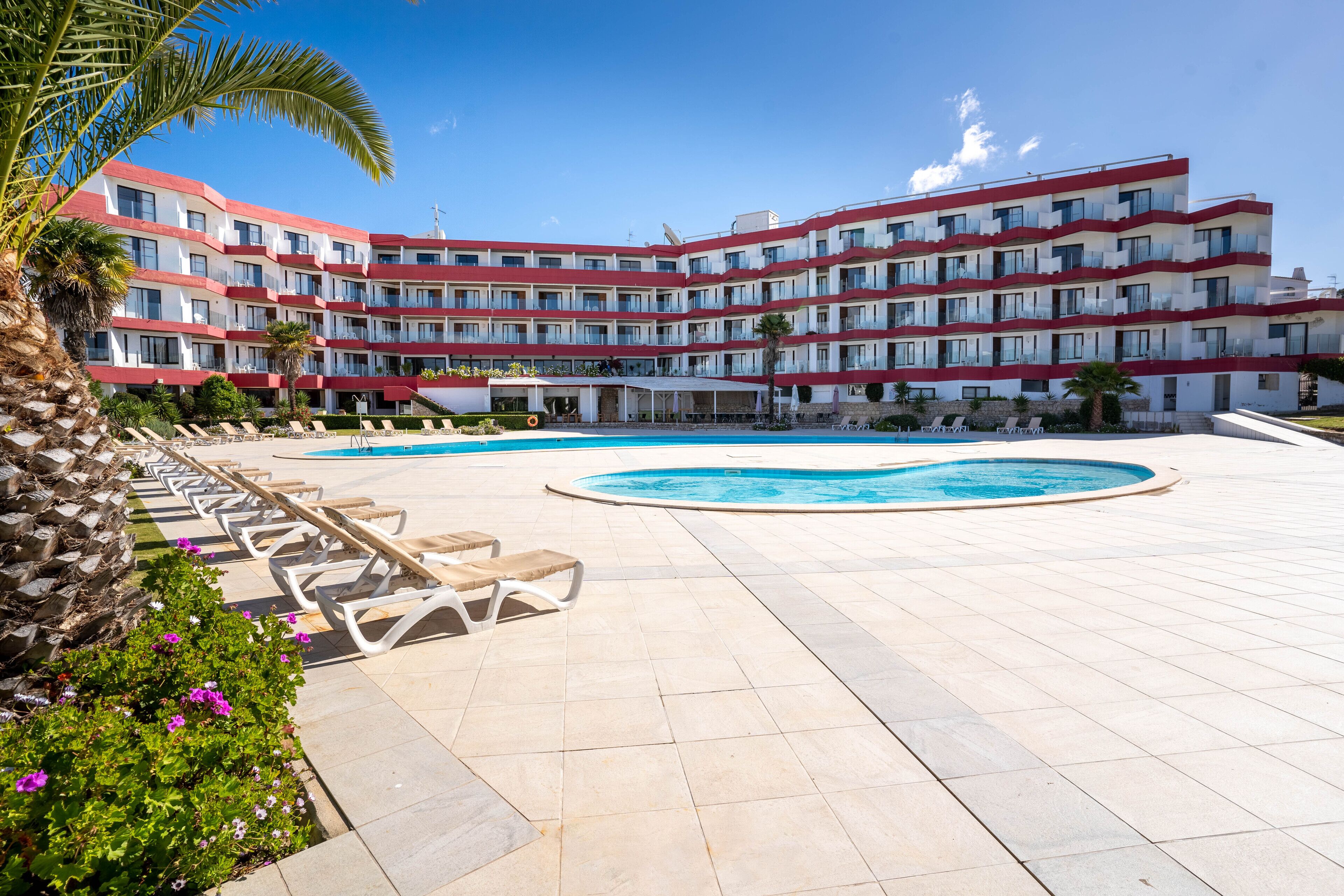 A hotel with a pool area, multiple balconies, and a clear blue sky.