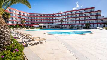 A hotel with a pool area, multiple balconies, and a clear blue sky.