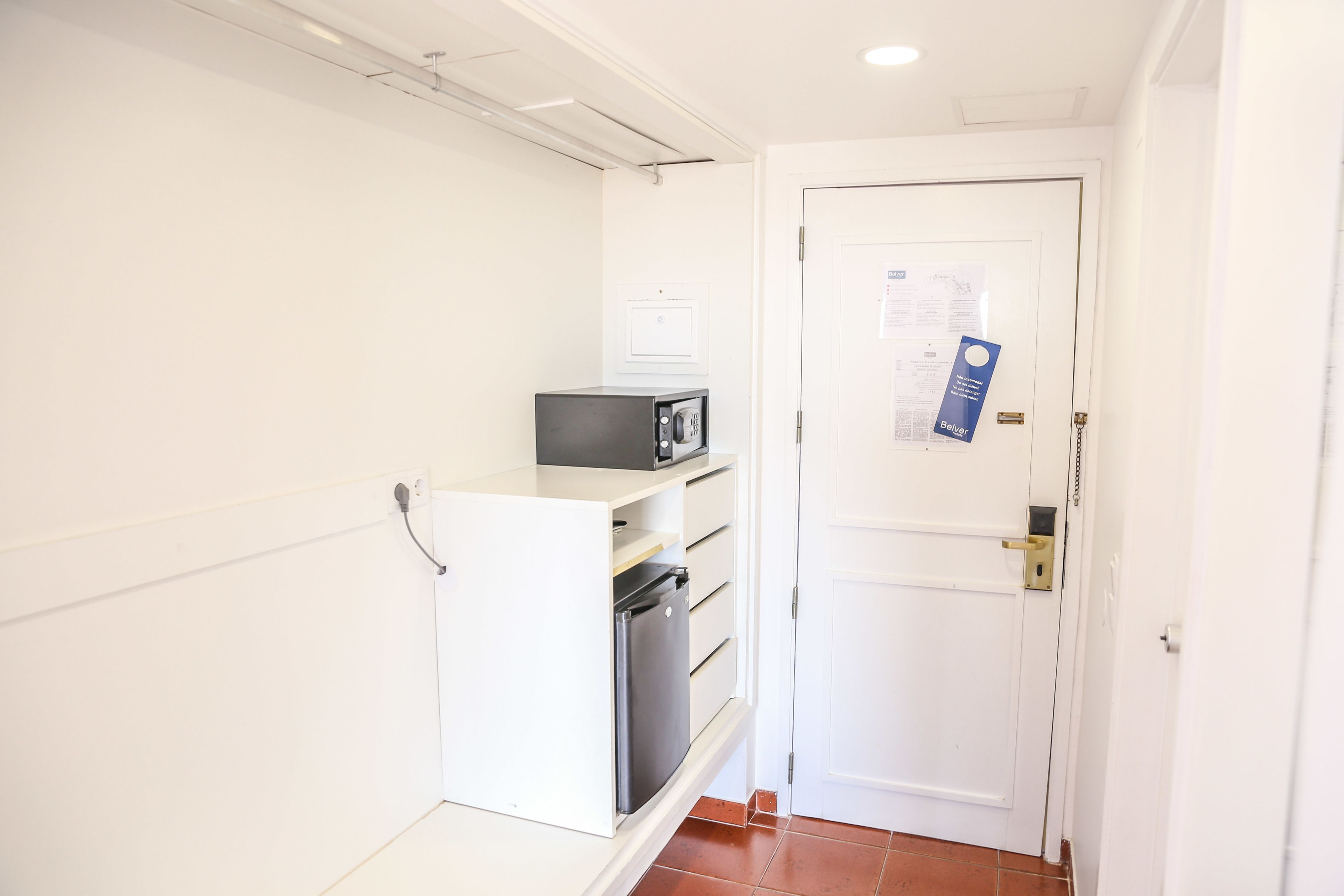 A narrow hallway with a white door, a small refrigerator, and a microwave on a shelf.