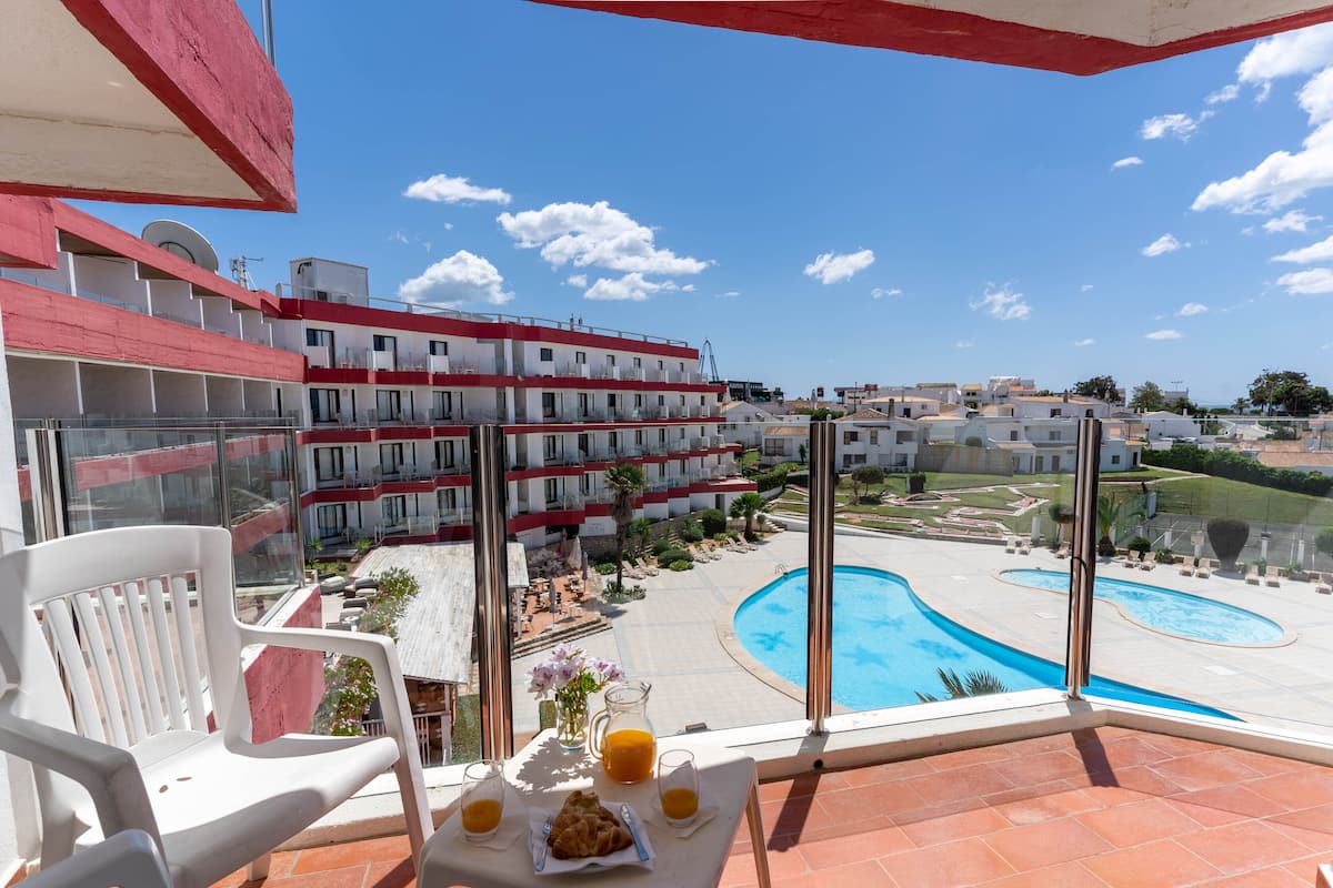 A balcony with a table set for breakfast, overlooking a swimming pool and a building complex.