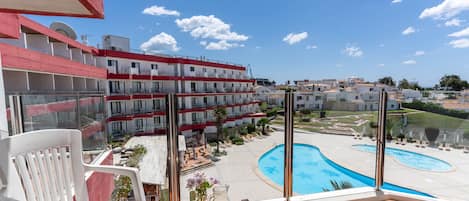 A balcony with a table set for breakfast, overlooking a swimming pool and a building complex.