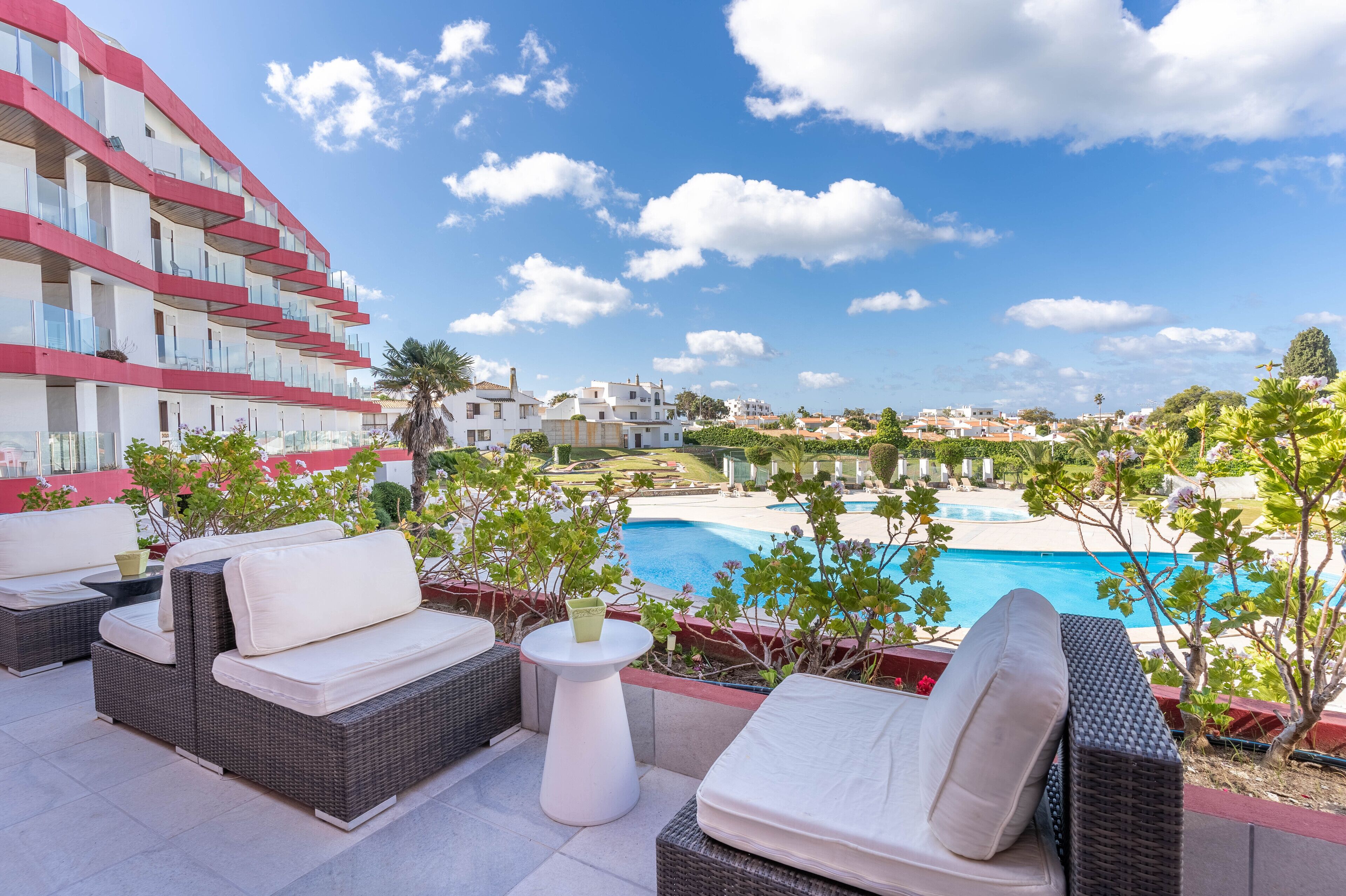 A rooftop terrace with wicker furniture, a pool, and a view of a residential area.