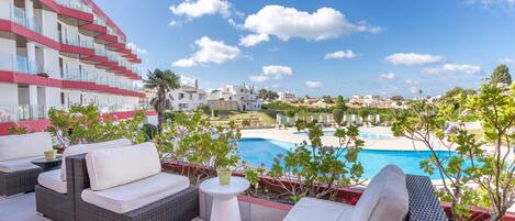 A rooftop terrace with wicker furniture, a pool, and a view of a residential area.