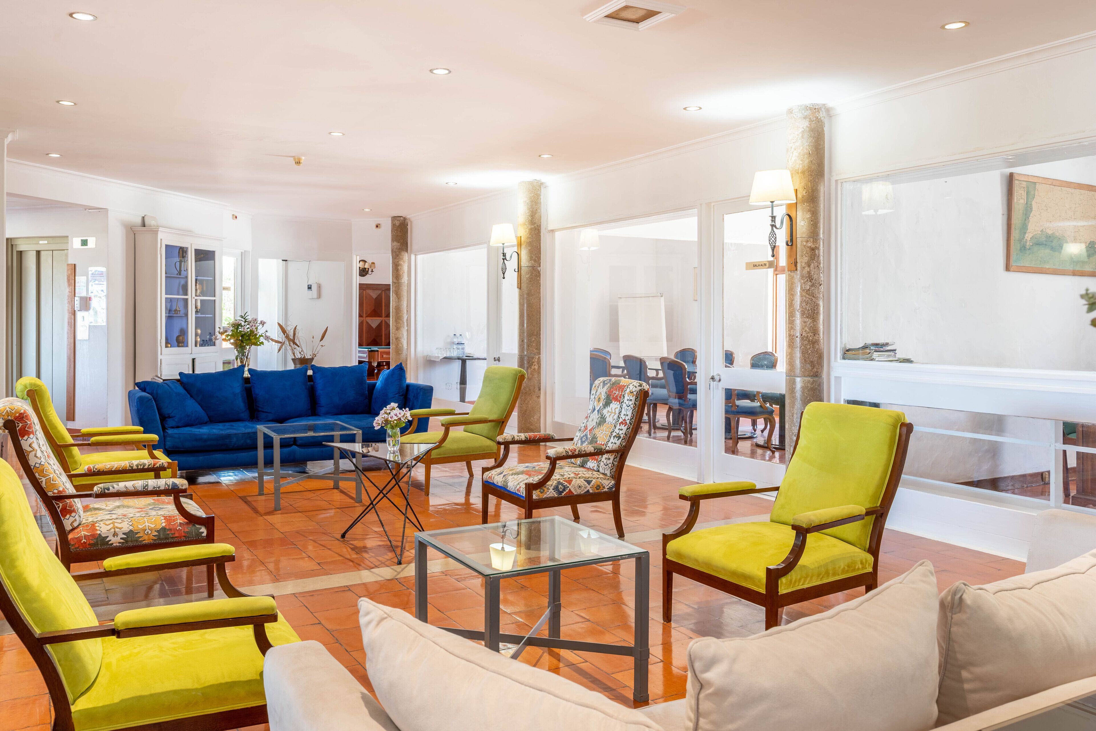Un salón amplio con un sofá azul, sillones verde y amarillo, y una mesa de centro de vidrio.
