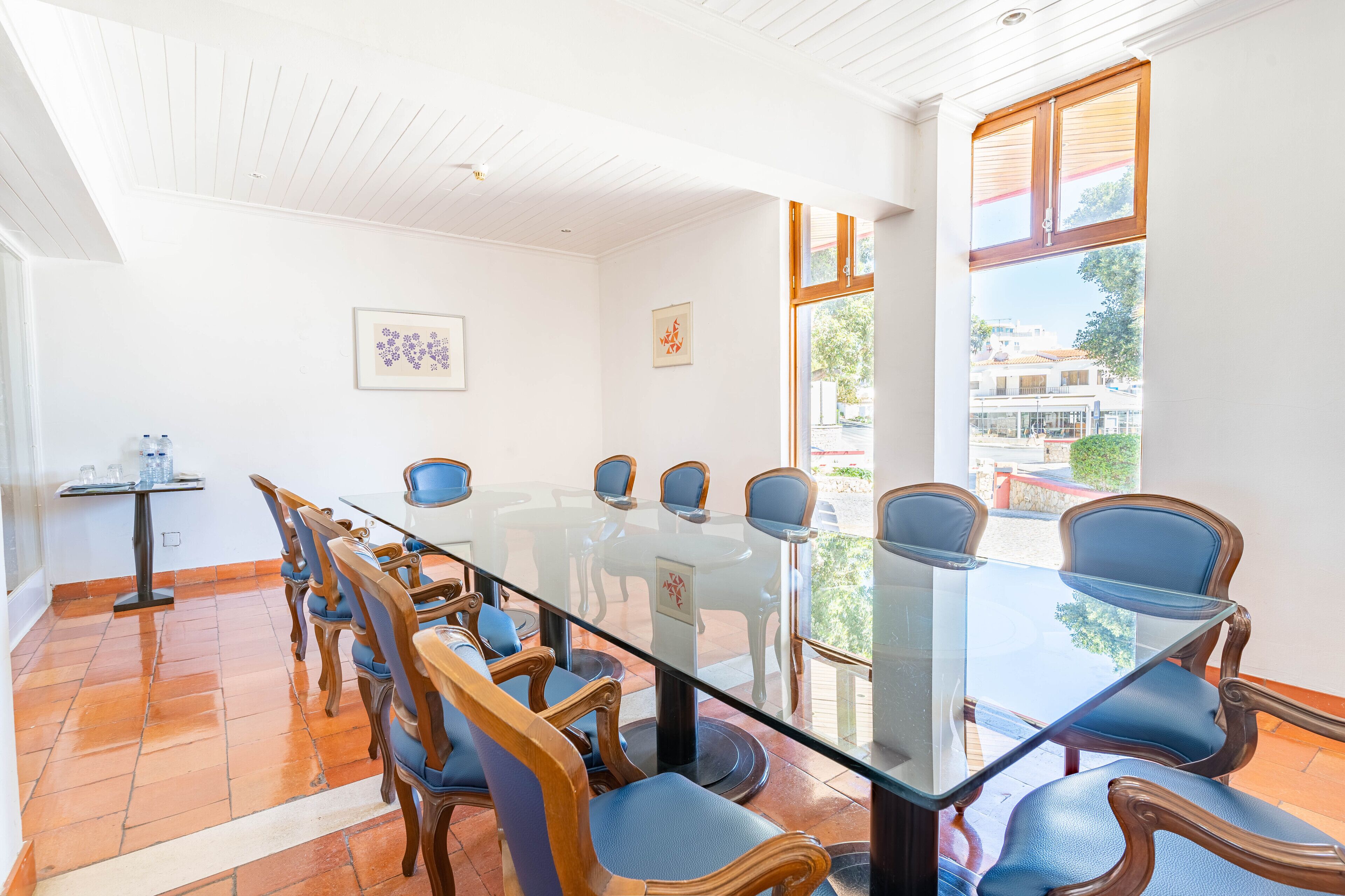 A conference room with a glass table and wooden chairs, a small table with water bottles, and a view of buildings outside.