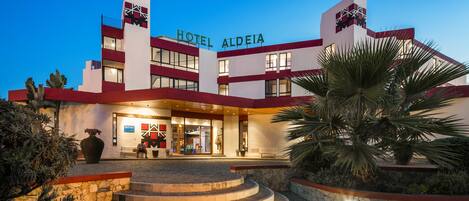A hotel with a modern design, featuring a prominent entrance with steps leading up to the main doors, and a well-lit facade.