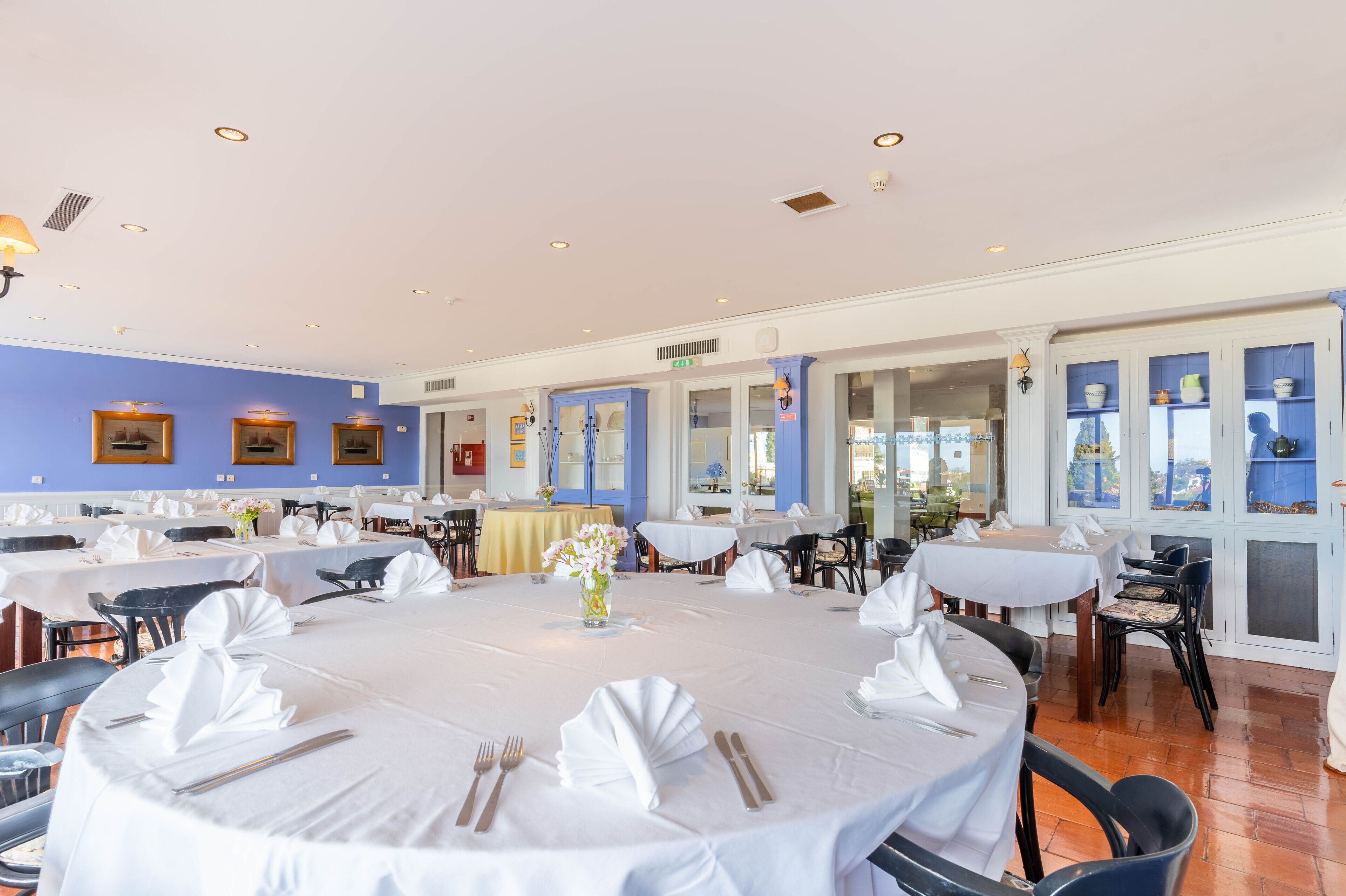 A large dining area with round tables set for multiple guests, featuring white tablecloths and neatly arranged cutlery.