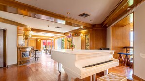 A grand piano in a spacious room with wooden floors, a bar area, and a large window. - Hotel da Aldeia - Adults Only (Albufeira)