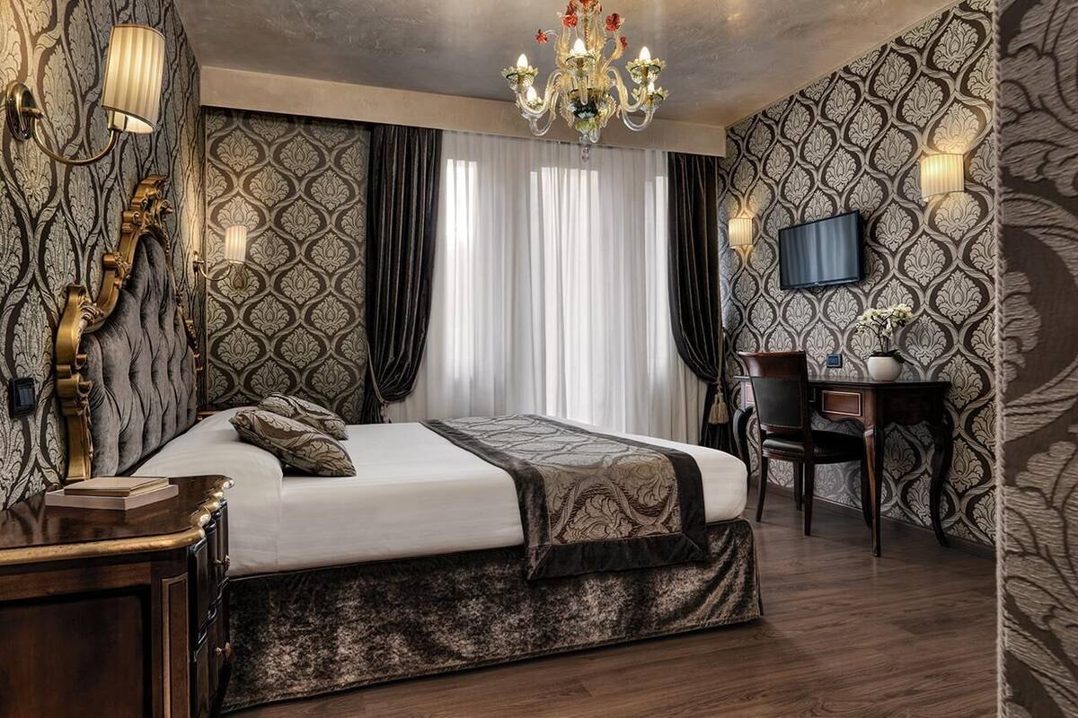 Une chambre d’hôtel avec un grand lit, un bureau, une télévision et un lustre.