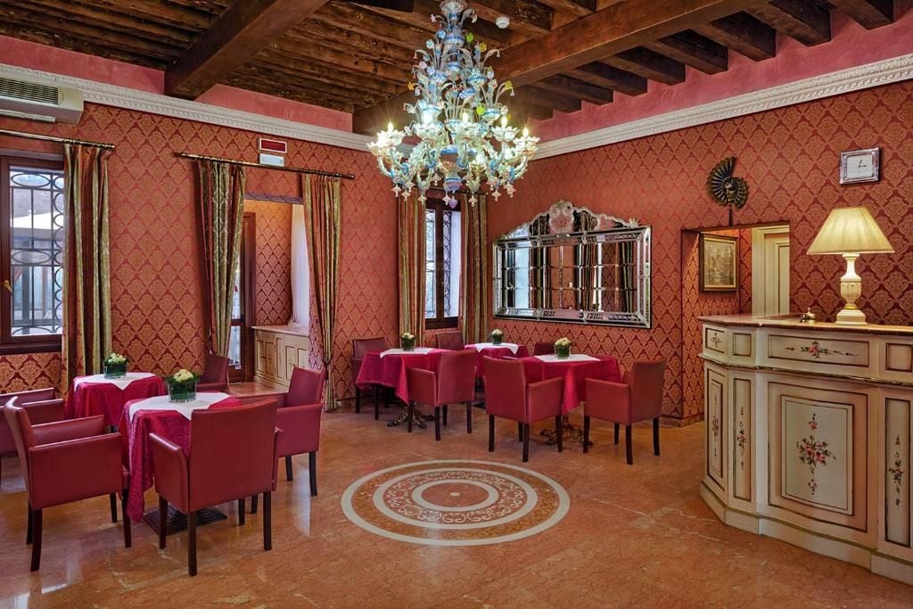A dining area with red chairs and tables, a chandelier, and a decorative mirror.