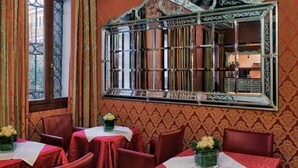 A room with a large ornate mirror, red patterned wallpaper, and multiple tables with red tablecloths and chairs. - Hotel Tre Archi (Venice)