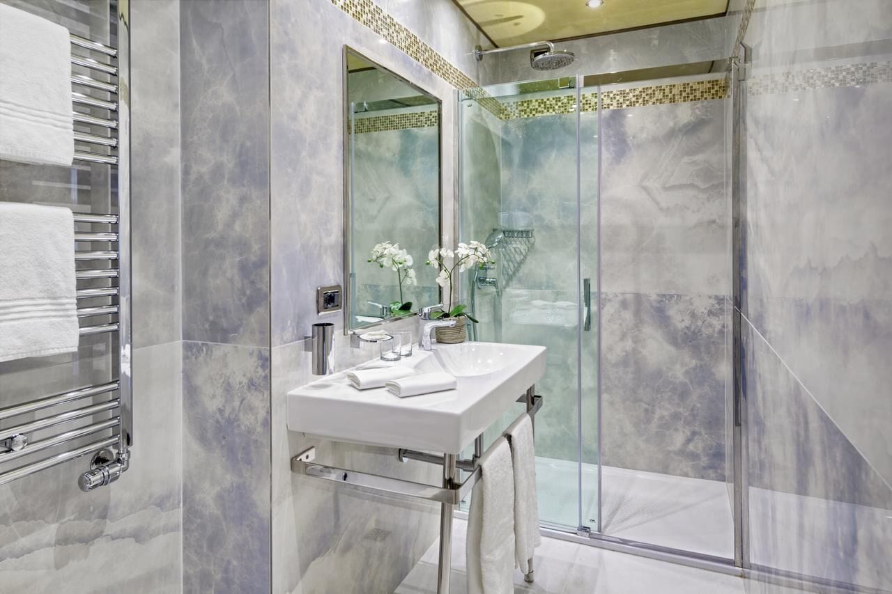 A modern bathroom with a glass shower enclosure, a white sink, and a towel rack.