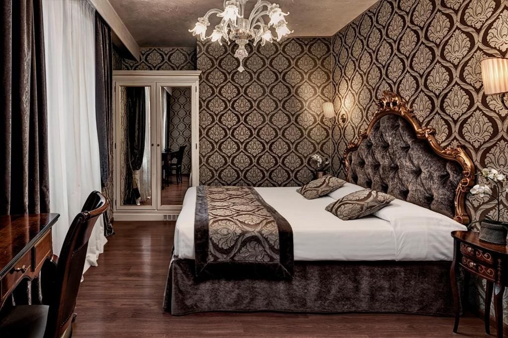 Quarto com cama grande, candelabro, papel de parede estampado e espelho.