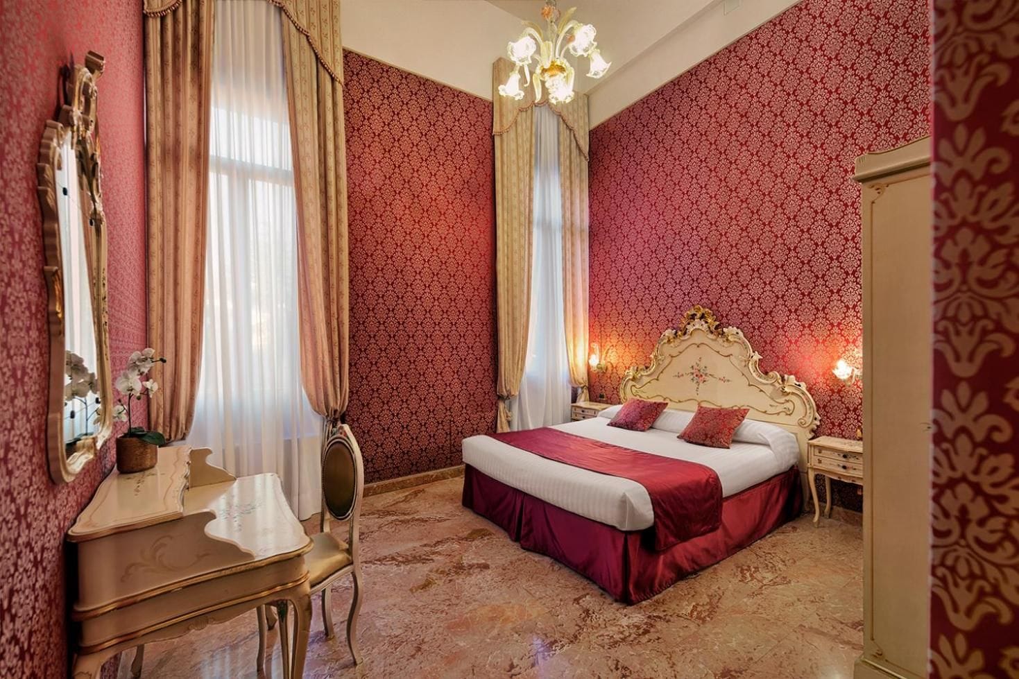 A bedroom with a large bed, a vanity with a mirror, and a chandelier.