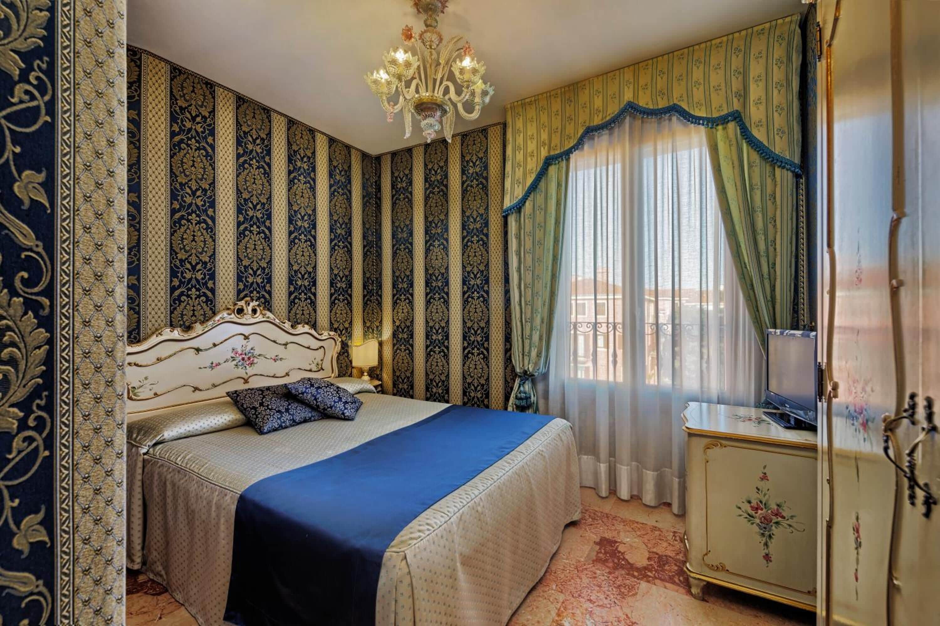 A bedroom with a large bed, a chandelier, a dresser, and curtains.