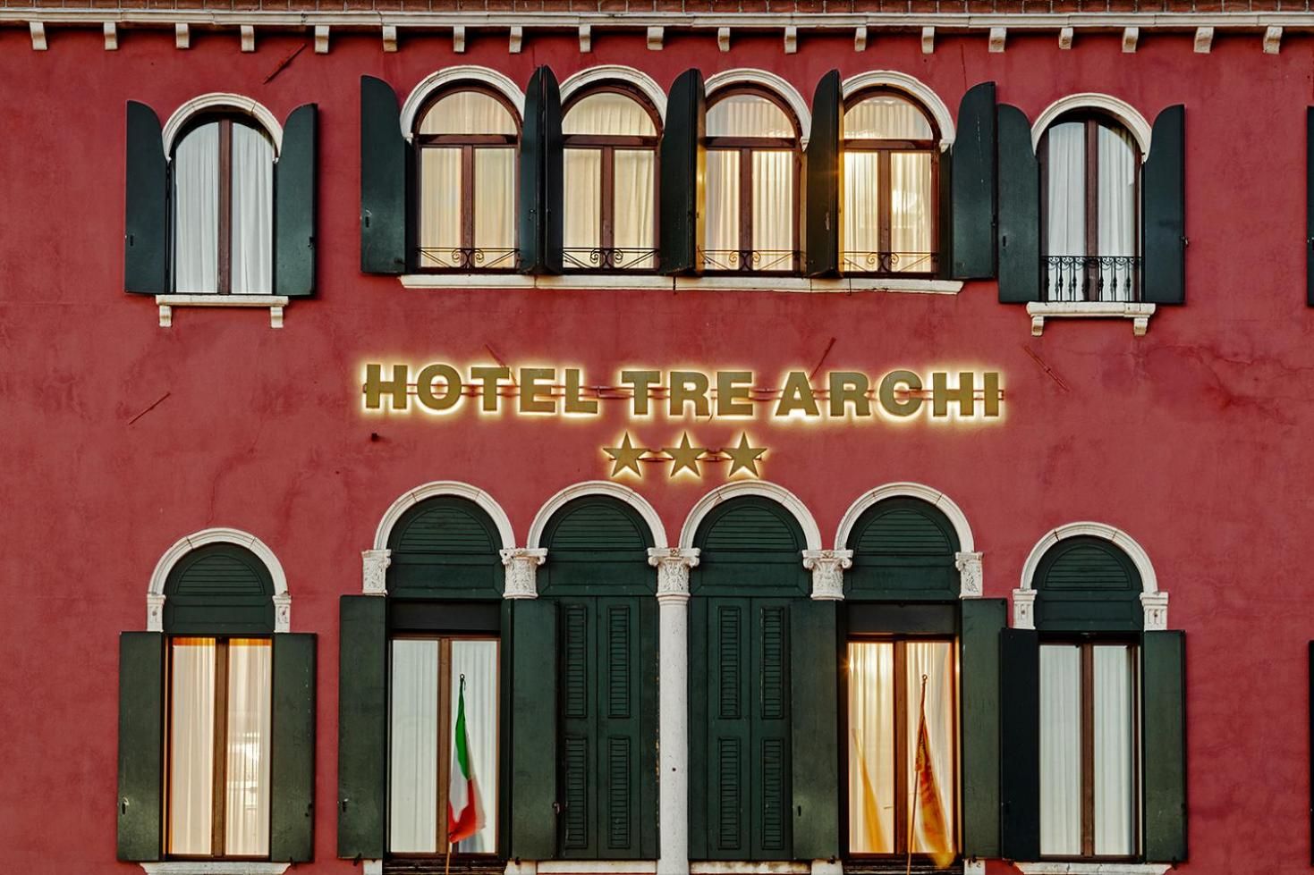 A building facade with multiple arched windows and a sign reading 'HOTEL TRE ARCH.'