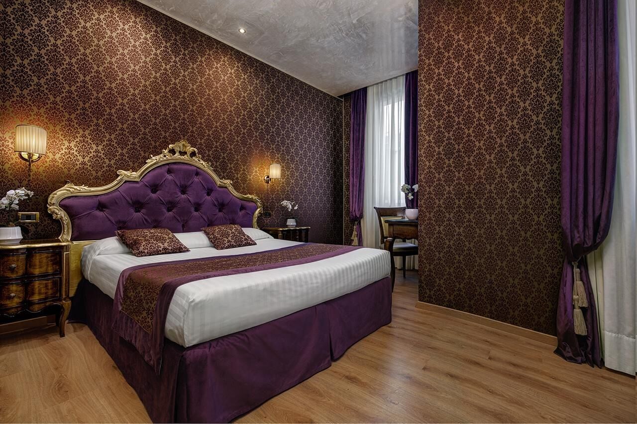 A bedroom with a large bed, ornate headboard, and patterned wallpaper.